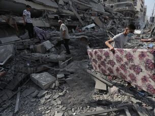 People stand amid the rubble of a building and looking at the ground. A man is carrying a large flower-patterned object.